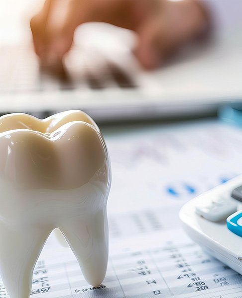 Large fake tooth next to a calculator on a desk with a hand on a laptop keyboard